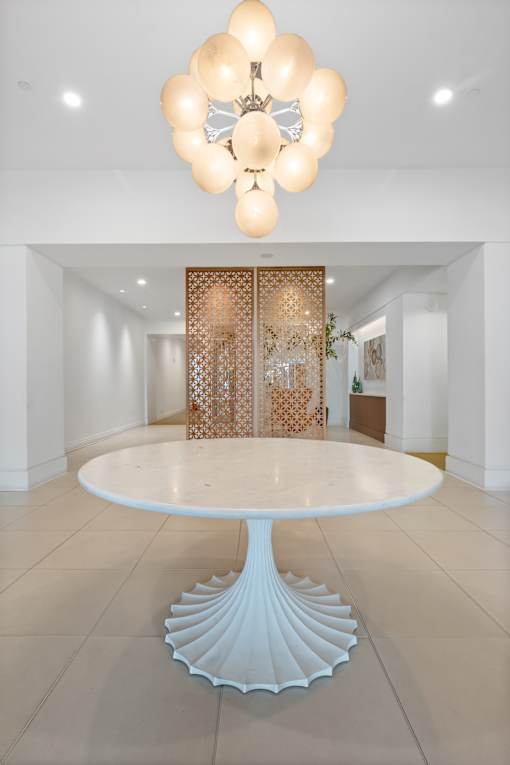 A white table with a flower-shaped chandelier hangs above it.