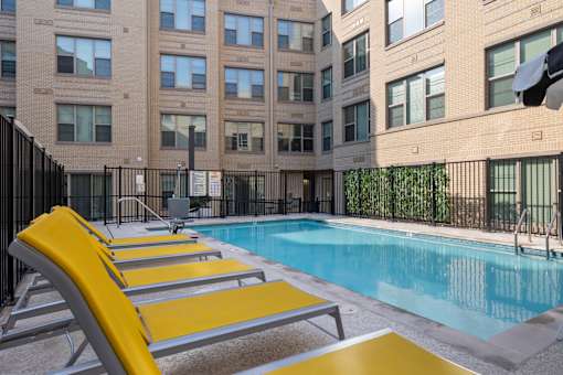 A pool with yellow sun loungers in front of a building.