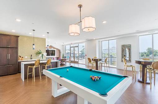 A pool table in a room with a kitchen area in the background.