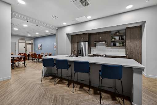 A modern kitchen with a long white island and blue chairs.