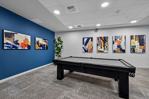 A pool table in a room with blue walls and abstract paintings on the wall.