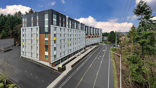 A modern multi-story building with a parking lot in front.