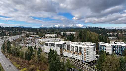A large white building with a blue roof is in the center of a parking lot.