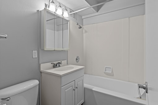 A white bathroom with a sink, mirror, and bathtub.