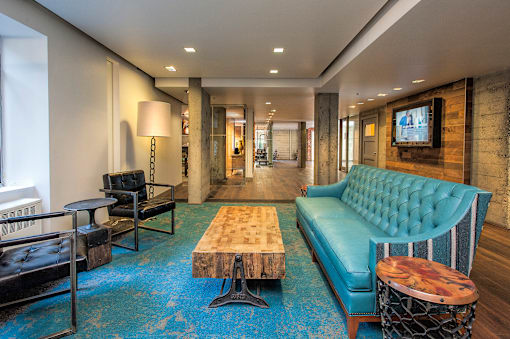 A blue couch sits in a room with a wooden table and a TV mounted on the wall.