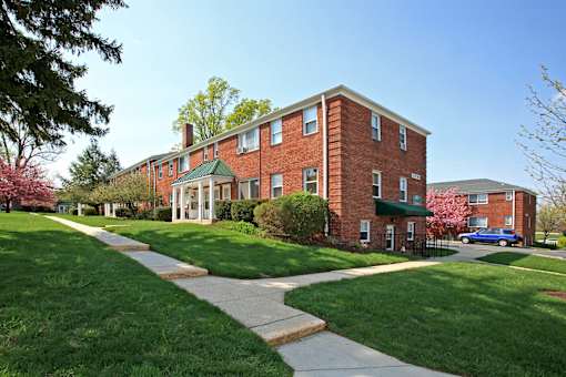 A red brick building with a green roof and a tree with pink flowers in front.