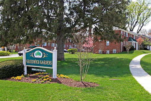 A sign for Greenwich Gardens is in the foreground of a well kept lawn.