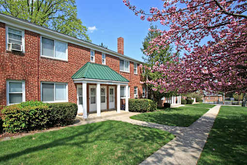 A red brick building with a green roof and a tree with pink flowers in front.