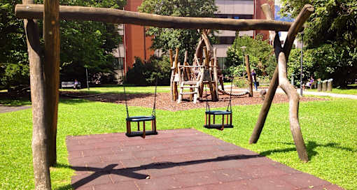 A swing set in a park with a red brick building in the background.