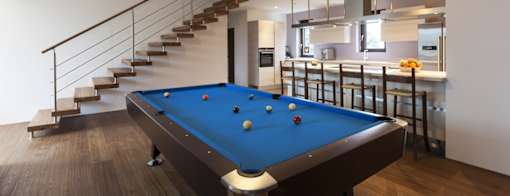 A pool table is in the middle of a room with a staircase.