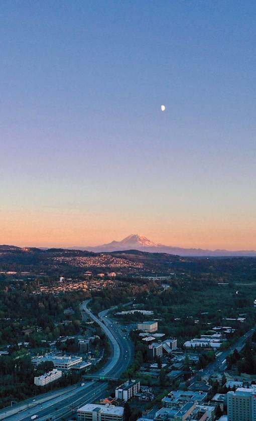 A cityscape with a mountain in the background and a crescent moon in the sky.
