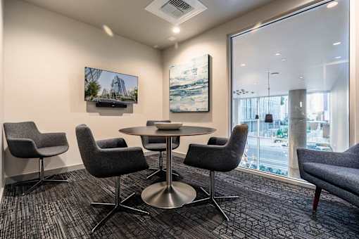 A conference room with a table surrounded by chairs and a television on the wall.