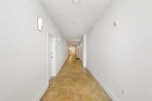 A long hallway with white walls and a light brown floor.