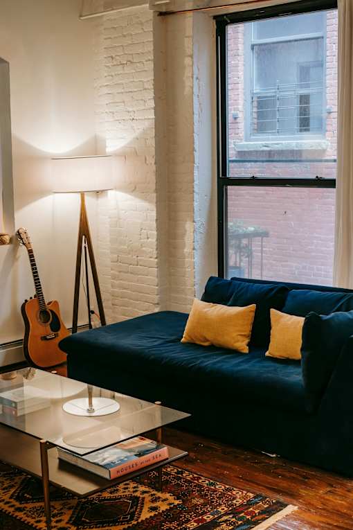A living room with a blue couch and a guitar hanging on the wall.