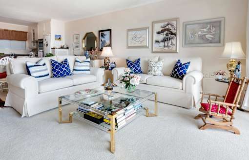 A living room with a white couch, a glass coffee table, and a wooden rocking chair.