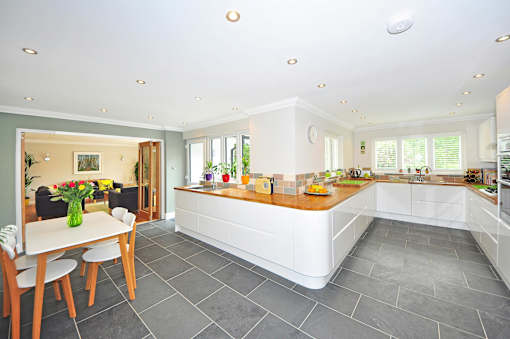 A kitchen with a table and chairs in the foreground and a countertop with a vase of flowers on it.