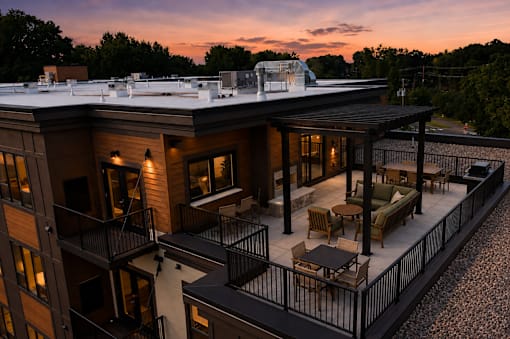 A rooftop patio with a table and chairs overlooks a forested area.