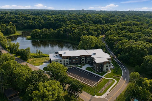 A large white building with a grey roof is surrounded by a forest.