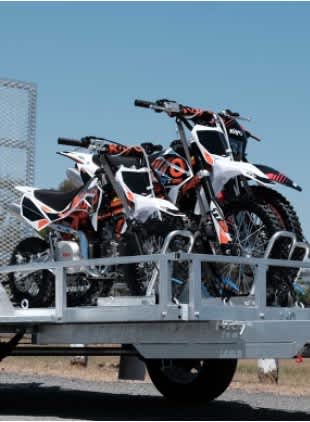 A trailer loaded with four motorcycles is parked.