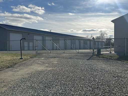 A gravel area in front of a grey building with a fence and gate.