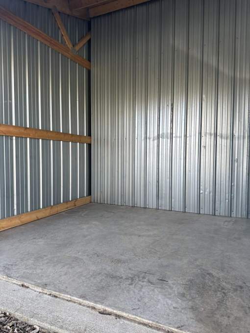 A large empty room with a grey floor and a corrugated metal wall.