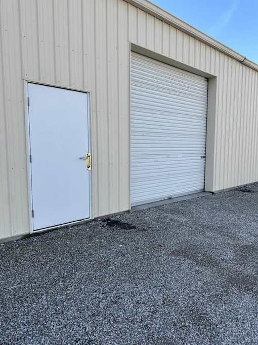 A white door with a gold handle is closed and attached to a grey building.