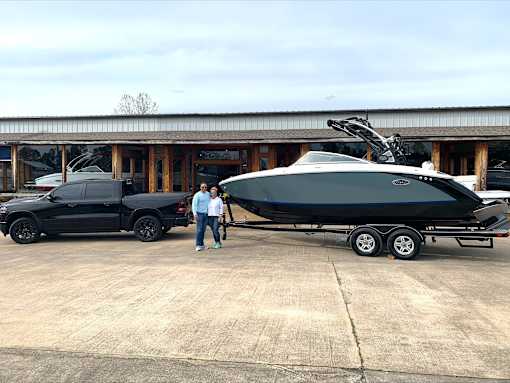 Two men stand next to a black boat and a black truck.
