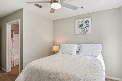 A bedroom with a bed, a ceiling fan, and a painting on the wall.