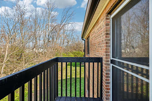A balcony with a black railing and a view of a green lawn and trees at Grand Valley Apartments, Milford, OH