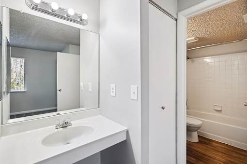 A white bathroom with a sink, mirror, and toilet at The Reserve at Grand Valley Apartments, Milford, OH