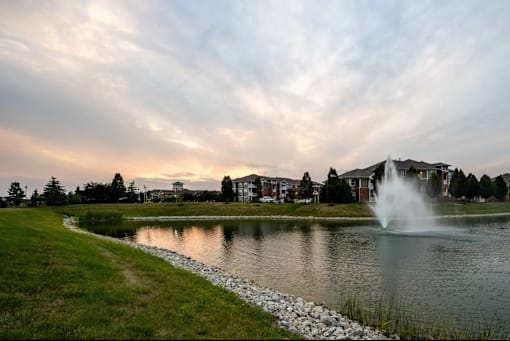 A fountain in the middle of a lake surrounded by grass.