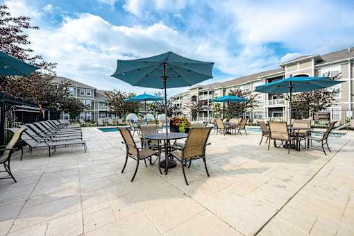 A patio with chairs and umbrellas is surrounded by buildings.