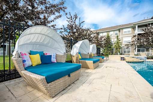 A poolside lounge area with white wicker chairs and cushions.
