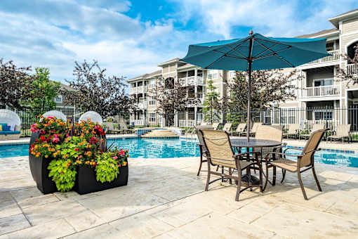 A patio with a table and chairs and a pool in the background.