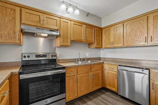 Irvine Park Towers apartment kitchen with wood cabinetry, light countertops and white appliances