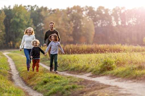 A family of four is walking down a dirt road holding hands.