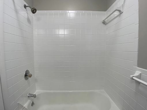 A white tiled bathroom with a white bathtub and shower.