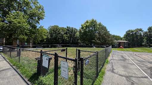 A grassy field surrounded by a fence with signs advising the entrance to a dog park.