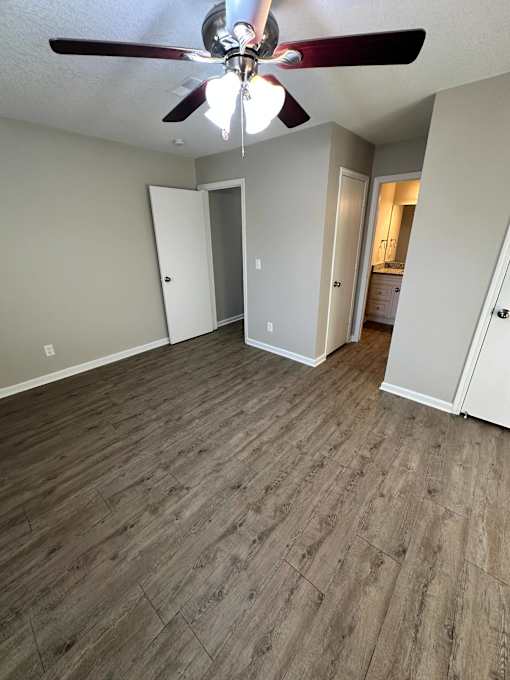 A room with a ceiling fan and light fixture, and wood flooring.
