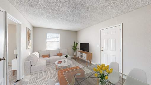 A living room with a grey couch, a coffee table, a television, and a vase of yellow flowers.