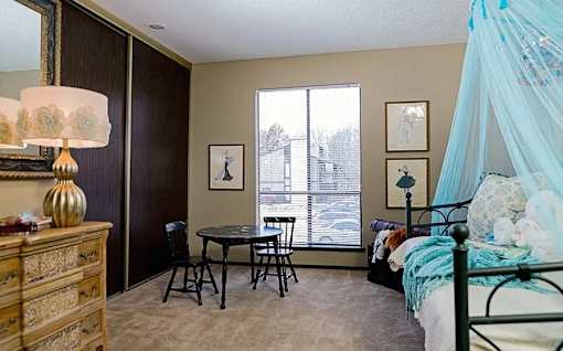 A bedroom with a bed, a dresser, a table, and chairs.