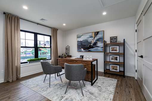A room with a desk, chairs and a painting on the wall.