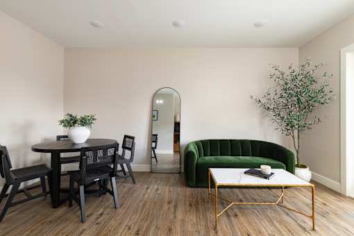 A living room with a green sofa, a round table with chairs, and a coffee table with a plant on it.