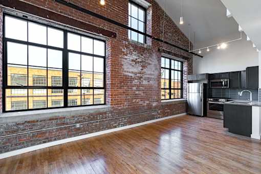 A large empty room with wooden floors and a brick wall.