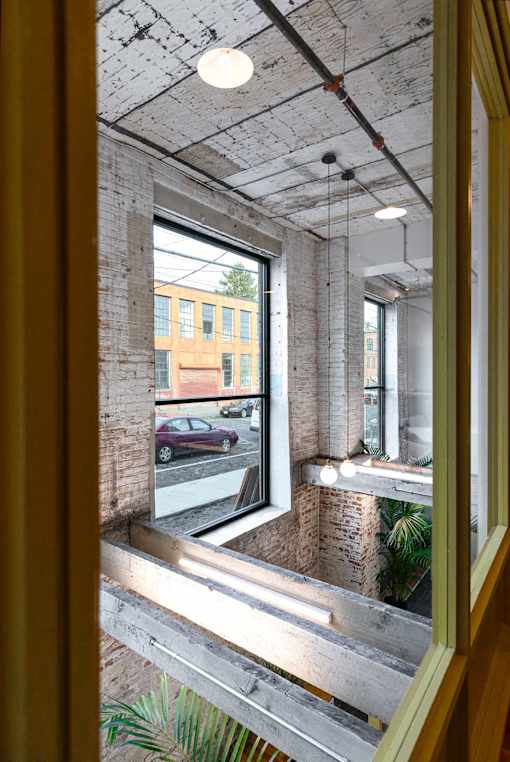 A view from inside a building looking out through a window at a red car and a building with a yellow facade.