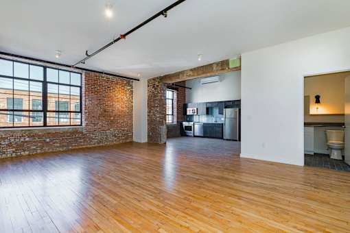 A large empty room with wooden floors and a brick wall.