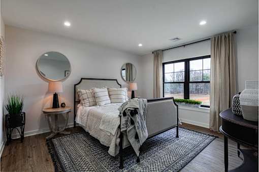 A bedroom with a bed, a side table with a lamp, and a window with a view of trees.