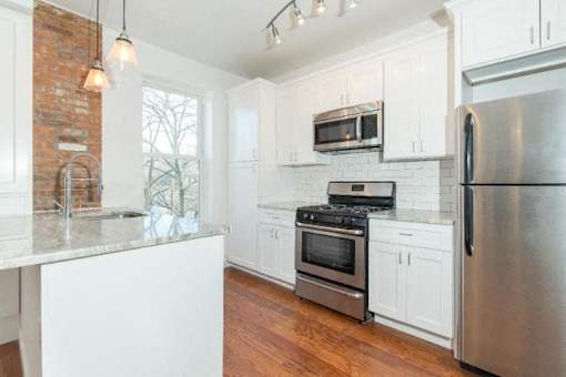 A kitchen with white cabinets and a brick wall.