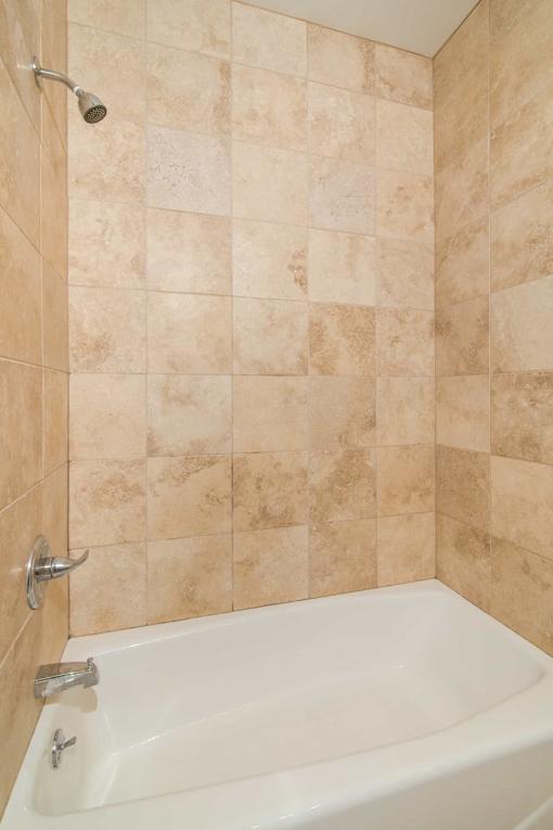 A white bathtub with a shower head and a tile wall.