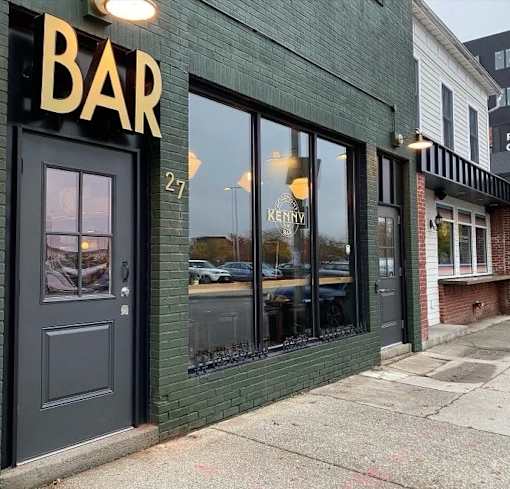 A bar with a black door and windows has a sign that says "Bar.".